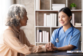 A nurse holding the hand of an elderly woman